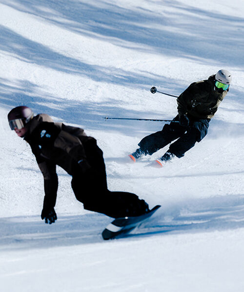 A skier and snowboarder riding down a mountain