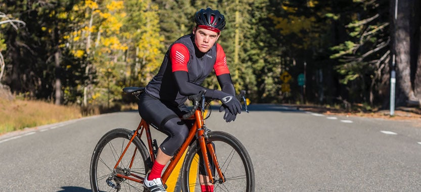 Man posing on a bicycle in a black and red helmet and jersey