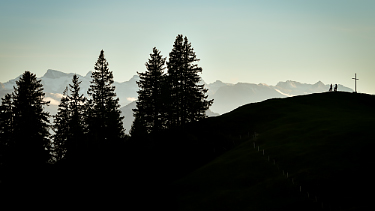 A silhouette of Amanda and Kathy taking a break at the top of a hill, with cloud-covered mountains looming behind them.